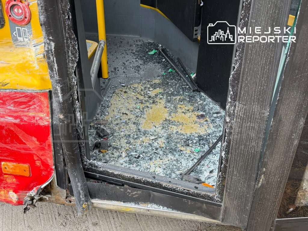 Rozbite drzwi autobusu z żółto-czerwonym nadwoziem, a na podłodze kabiny rozsypane odłamki szkła.