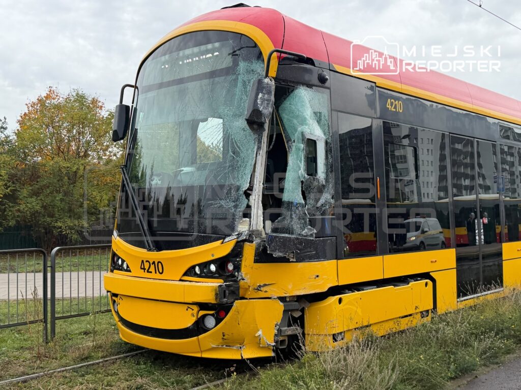 Uszkodzony tramwaj z rozbitą przednią szybą i wgniecionym przodem stoi przy torowisku obok trawiastego pobocza.