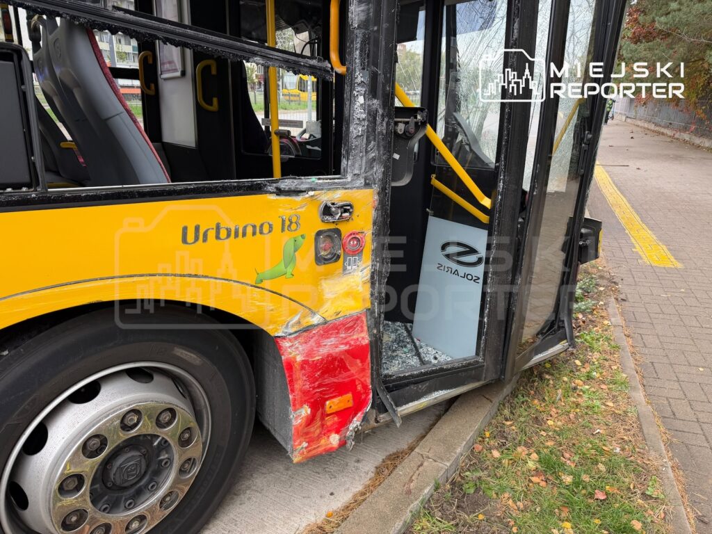 Żółty autobus miejski z uszkodzonym tylnym bokiem i otwartymi drzwiami stoi przy krawężniku.