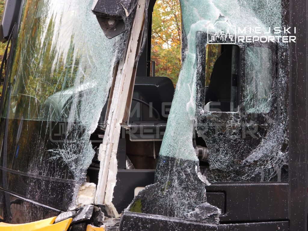 Rozbita przednia szyba autobusu, z widocznym wnętrzem pojazdu i uszkodzoną karoserią.