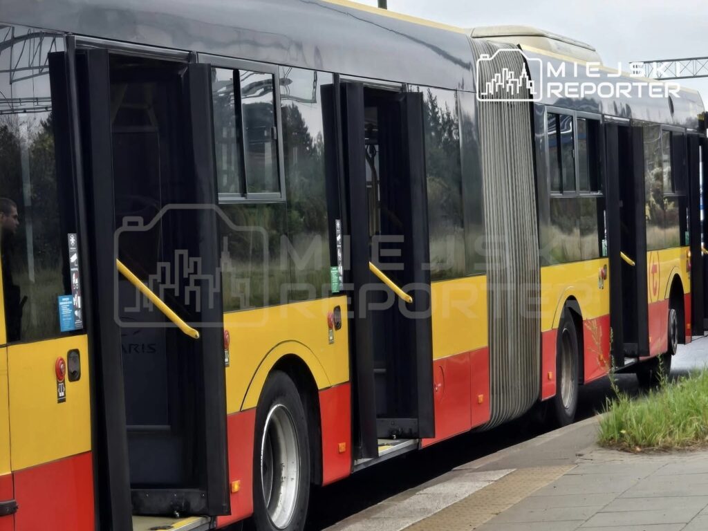 Przegubowy autobus miejski z żółto-czerwonym nadwoziem stoi przy chodniku z otwartymi drzwiami.