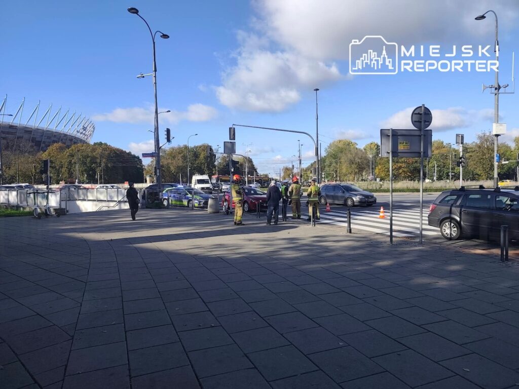 Strażacy i policjanci zabezpieczają miejsce zdarzenia na skrzyżowaniu, obok stoją samochody i radiowóz.