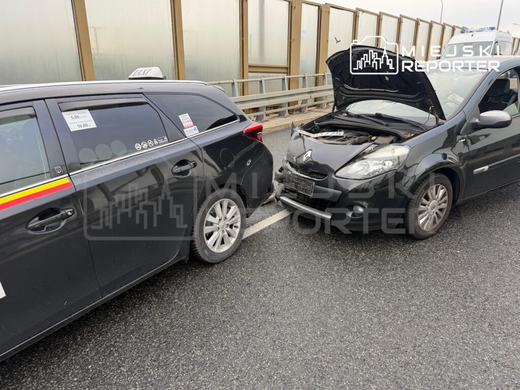 Uszkodzone auto z otwartą maską uderza przodem w tył oznakowanego radiowozu na jezdni przy ekranach akustycznych.