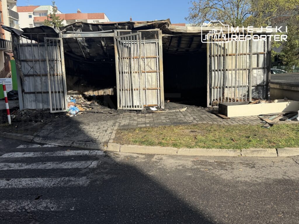 Spalona altana z poczerniałym, zapadniętym dachem i otwartymi metalowymi bramami przy chodniku.