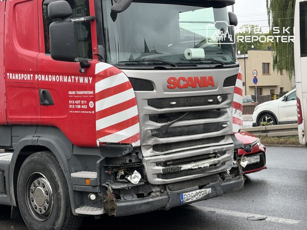 Uszkodzona ciężarówka Scania stoi na jezdni; za nią widać przód czerwonego auta osobowego.