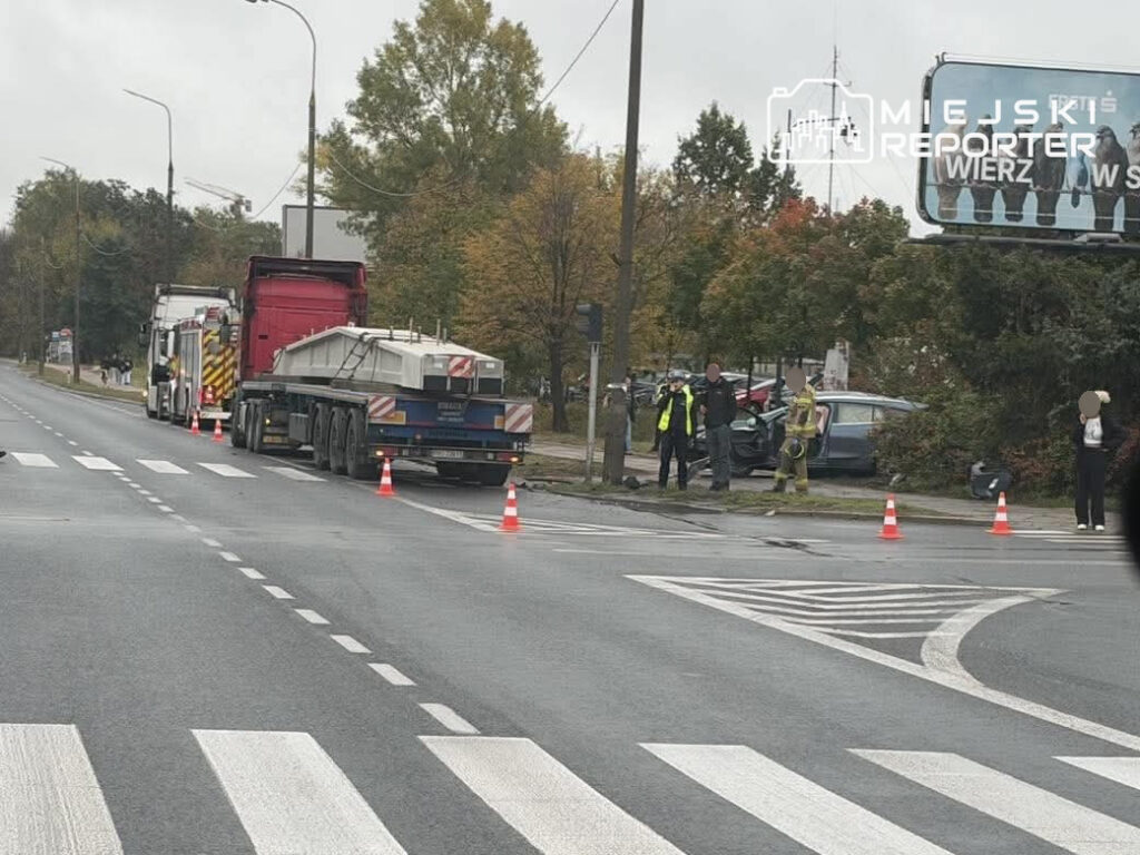 Strażacy i policjanci zabezpieczają miejsce zdarzenia przy drodze, obok ciężarówek i samochodu osobowego.