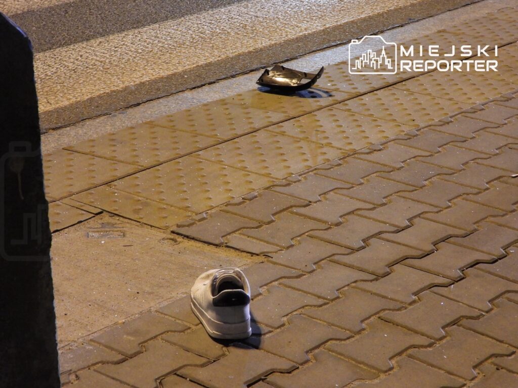 Samotny dziecięcy but leży na chodniku z kostki brukowej, obok metalowego elementu.