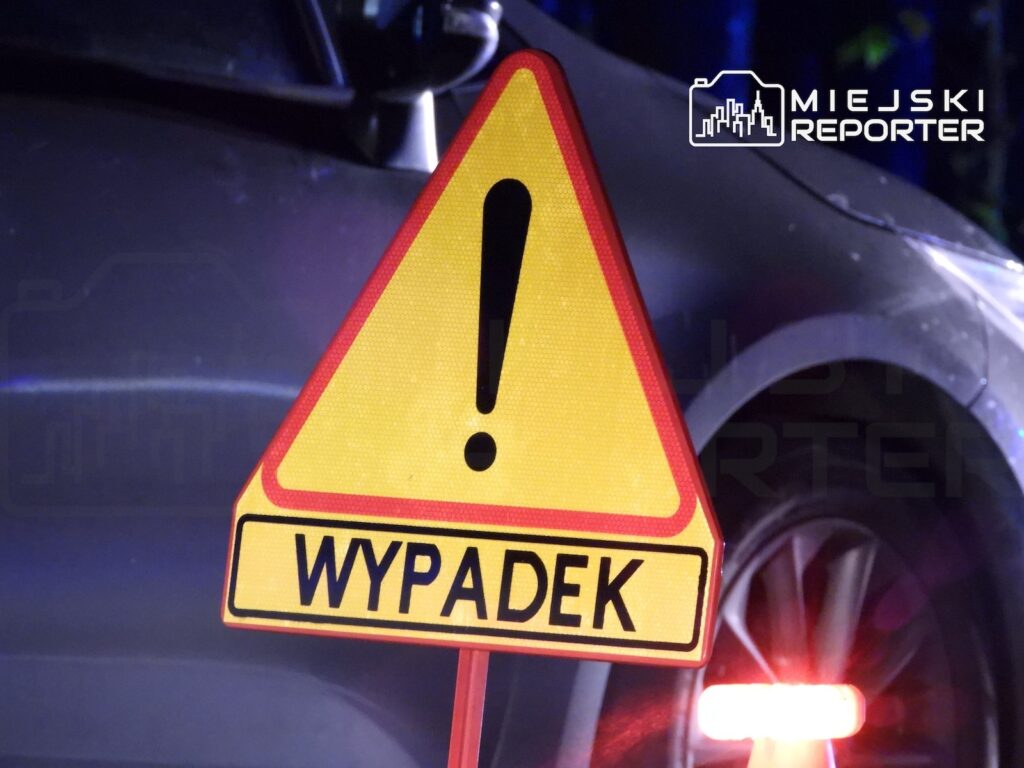 Trójkątny znak ostrzegawczy z wykrzyknikiem i napisem „WYPADEK” na tle samochodu.