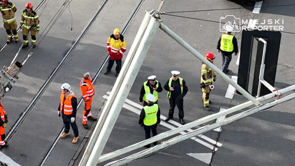 Służby ratunkowe i pracownicy w kamizelkach odblaskowych stoją przy torowisku tramwajowym pod uszkodzoną konstrukcją