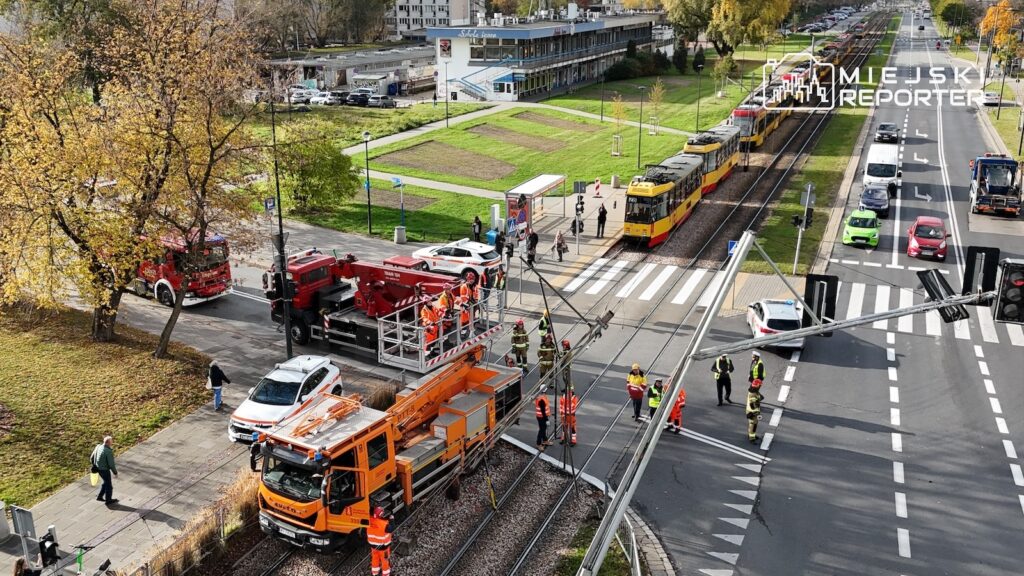 Strażacy i pojazdy ratunkowe na torowisku tramwajowym przy ruchliwej ulicy, obok zatrzymanego tramwaju.