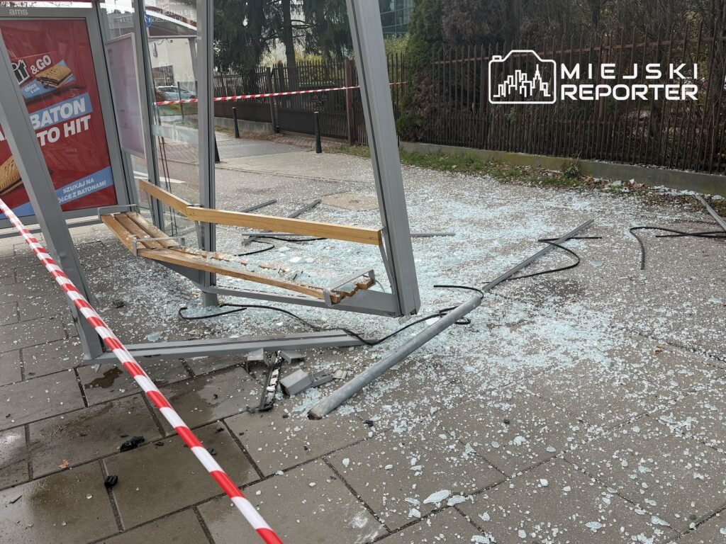 Uszkodzona wiata przystankowa z rozbitymi szklanymi panelami i rozsypanym szkłem, odgrodzona taśmą ostrzegawczą
