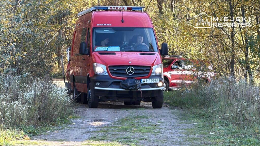 Czerwony samochód straży pożarnej stoi na leśnej drodze wśród jesiennych drzew.