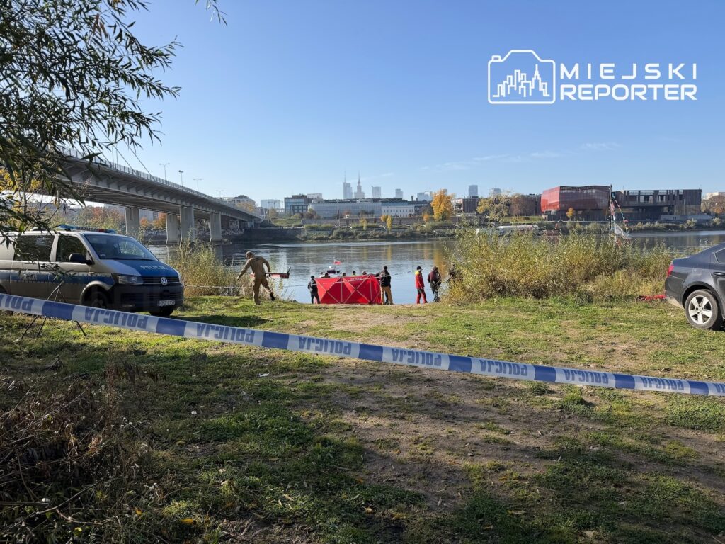 Policjanci pracują przy czerwonym namiocie nad rzeką; teren odgrodzono taśmą policyjną.