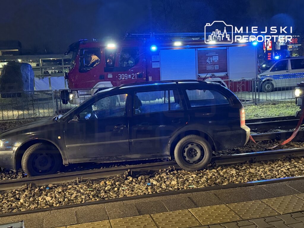 Ciemne kombi stoi na torach kolejowych, za nim straż pożarna i radiowóz z włączonymi światłami.