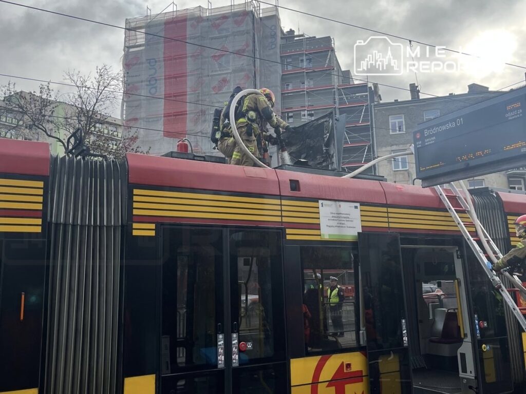 Strażak w sprzęcie ochronnym sprawdza dach tramwaju, na którym widać uszkodzoną, osmoloną instalację.