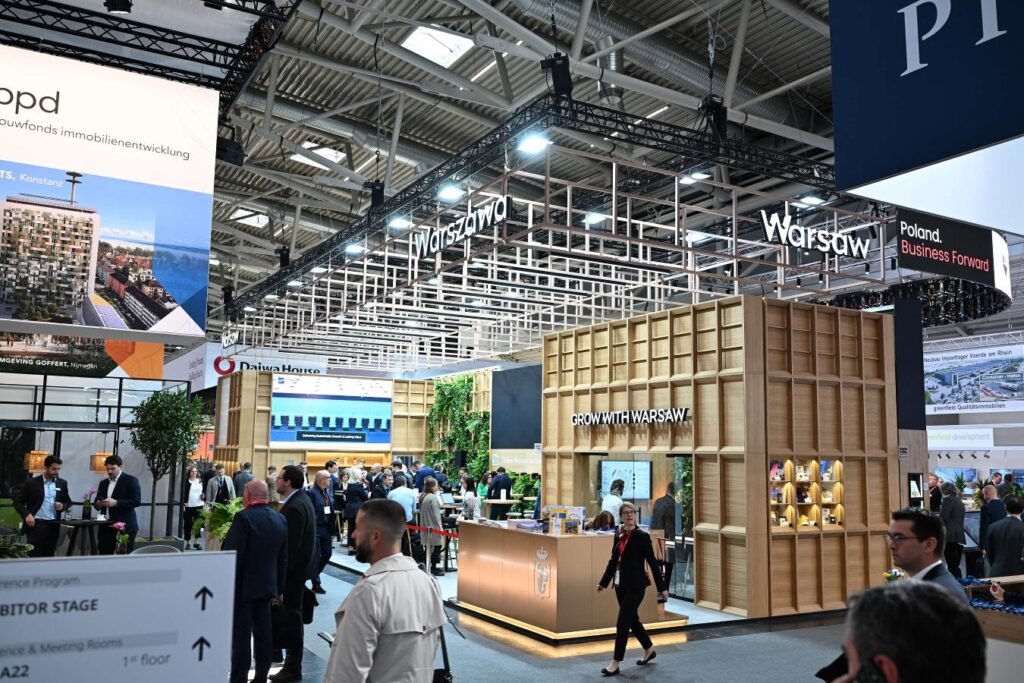 Stoisko „Warsaw” z napisem „GROW WITH WARSAW” i odwiedzający na targach nieruchomości EXPO REAL.